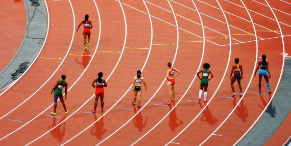 Acht Läuferinnen stehen auf einer roten Laufstrecke an der Startlinie.