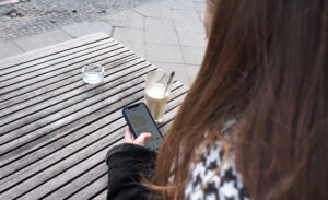 Eine Frau sitzt an einem Café-Tisch und schaut auf ihr Smartphone.
