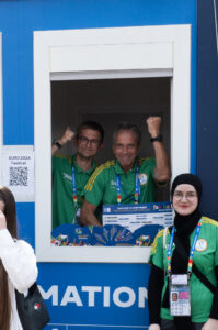 Drei Volunteers schauen aus dem Infostand in der Fanzone am Friedensplatz