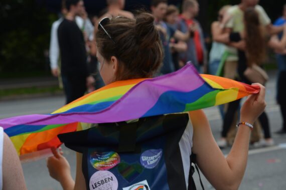 Eine von hinten zu sehende Frau hält eine Regenbogenfahne in der Hand, Foto: Pixabay, fsHH