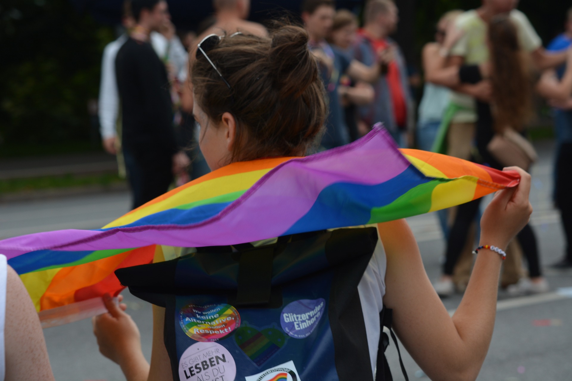 Eine von hinten zu sehende Frau hält eine Regenbogenfahne in der Hand