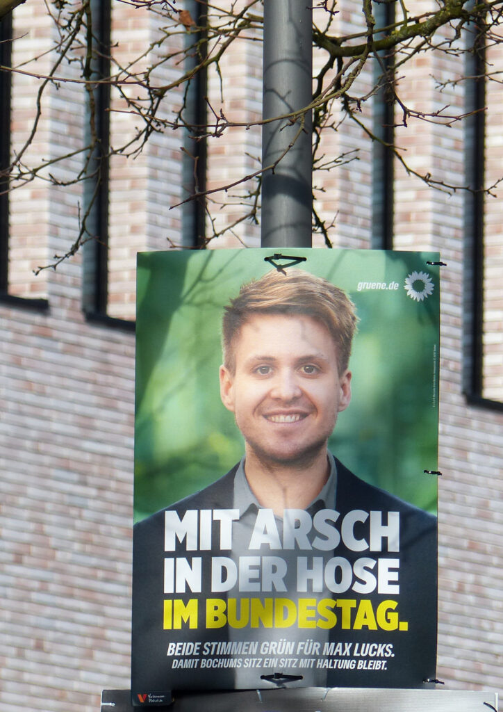 Ein Wahlplakat der Grünen mit dem Abgeordneten Max Lucks im Bild. Auf dem Plakat steht "Mit Arsch in der Hose in den Bundestag. Das Foto wurde vor dem Musikforum in Bochum aufgenommen.