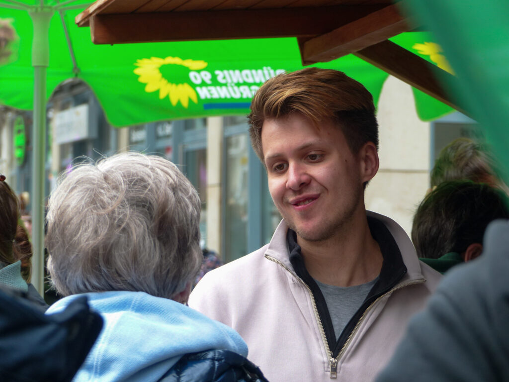 Max Lucks, Abgeordenter der Grünen, steht in der Bochumer Innenstadt und unterhält sich an einem Wahlkampfstand mit einer Frau.