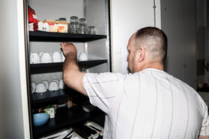 Mann(Abdul) räumt Tassen in Schrank
