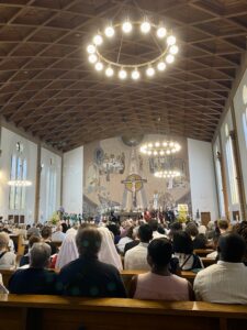 Die Kirchenbänke sind alle besetzt. Die Menschen stehen und blicken zum Altar.