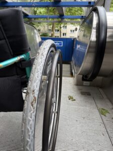 Ein Rollstuhl in Nahaufnahme, dahinter beginnt eine Rolltreppe.