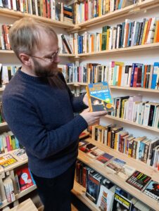 Der Inhaber steht vor Bücherregalen und hält ein Buch