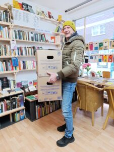 Weißer mittelalter Mann steht mit zwei Umzugskartons im Buchladen