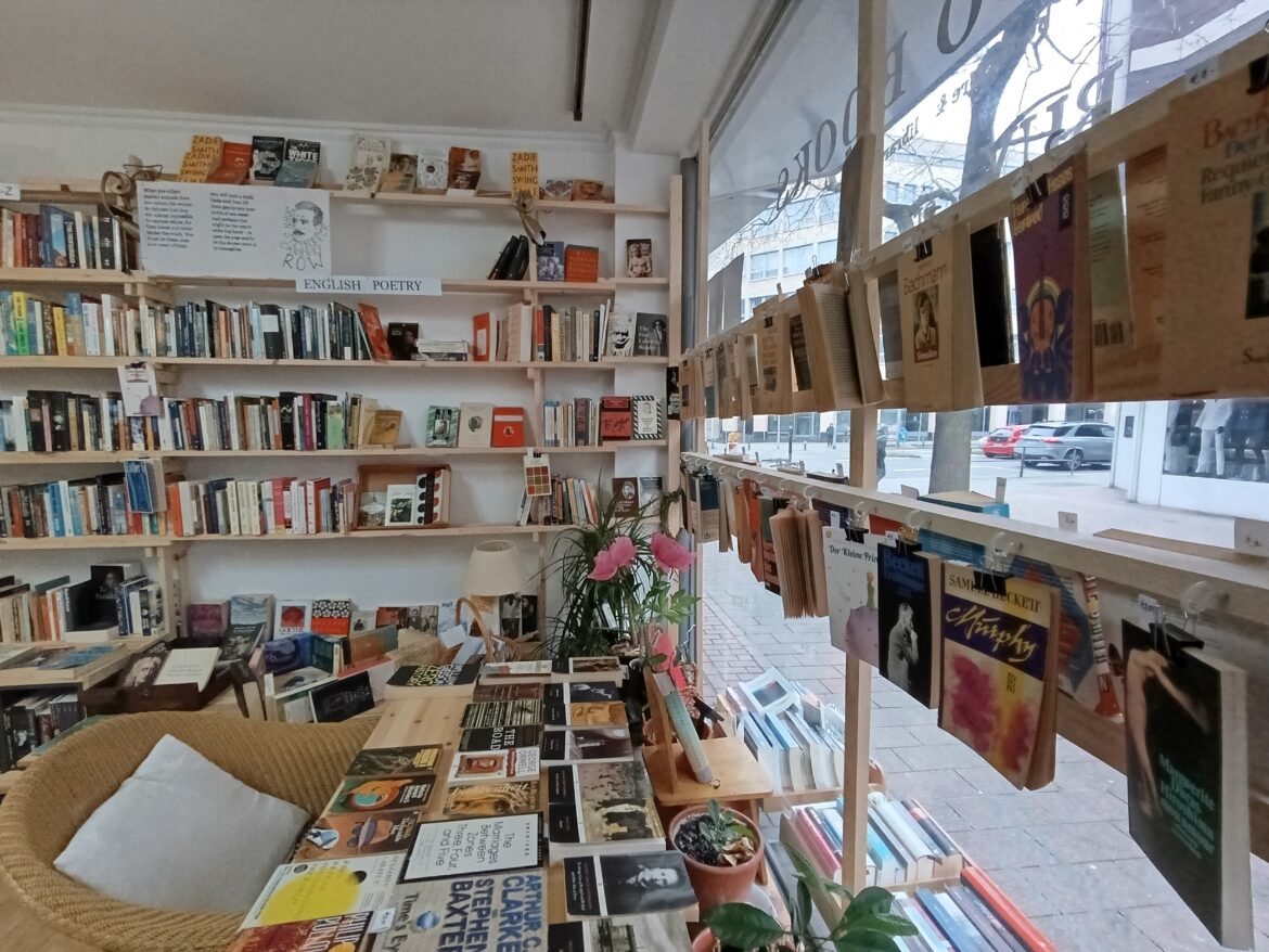 An einem Tisch mit Büchern steht ein Rattansessel mit weißem Kissen.