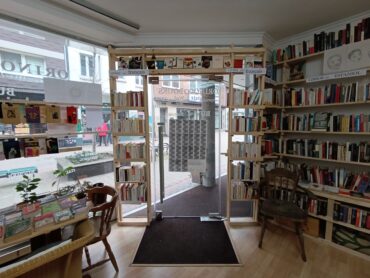 Blick von Innen auf die Ladentür des Orinoco. Die Glastür ist umgeben von Bücherregalen, die bis zur Decke gehen.