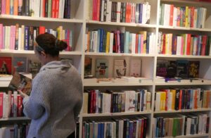 Kundin in einem grauen Pullover steht mit einem Buch in der Hand vor einem Regal.