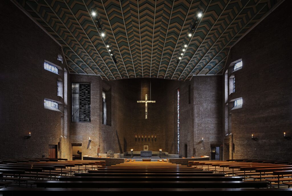 Beleuchteter Kirchenraum der Abteikirche Königsmünster mit Fokus auf Altarraum, Kirchenschiff und Kruzifix