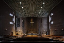 Beleuchteter Kirchenraum der Abteikirche Königsmünster mit Fokus auf Altarraum, Kirchenschiff und Kruzifix