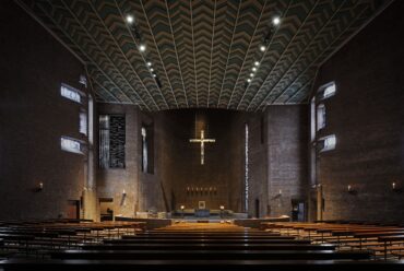 Beleuchteter Kirchenraum der Abteikirche Königsmünster mit Fokus auf Altarraum, Kirchenschiff und Kruzifix