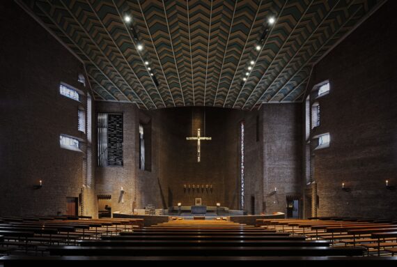 Beleuchteter Kirchenraum der Abteikirche Königsmünster mit Fokus auf Altarraum, Kirchenschiff und Kruzifix