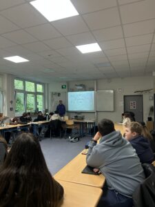 Die Schüler*innen der Klasse 7c sitzen in einem Klassenraum der Gesamtschule Höhscheid in Solingen. Ihr Lehrer, Peer-Boris Weichsel, steht neben einem digitalen Tafelbild vor der Klasse.