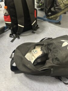 Ein schwarzer Rucksack einer Schülerin liegt geöffnet auf dem Boden eines Klassenraums der Gesamtschule Höhscheid in Solingen. In der Tasche ist ein Smartphone zu sehen.